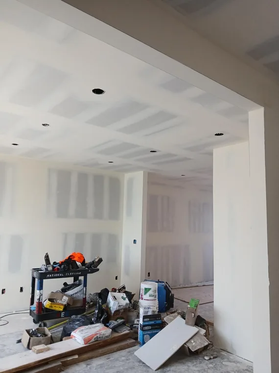 Room with taped drywall walls and ceiling, recessed light openings, tools and materials
