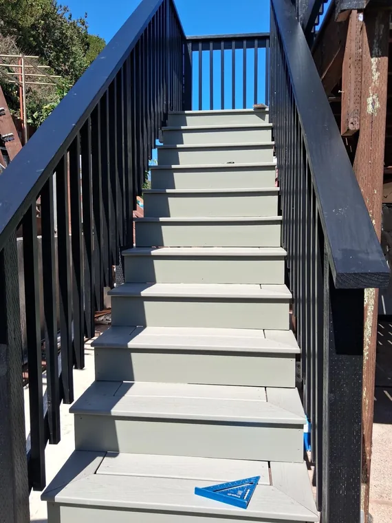 Gray exterior stair treads between black railings, with a blue framing square on a tread