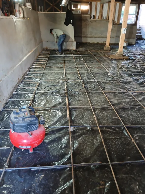 Worker beside a reinforcing steel grid over membrane in an unfinished lower-level room