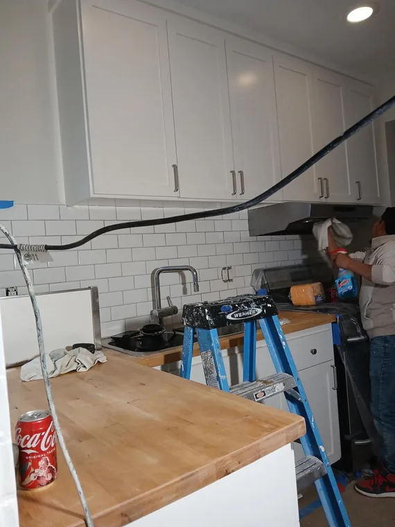 White kitchen cabinets and subway tile with a worker, ladder and tools present