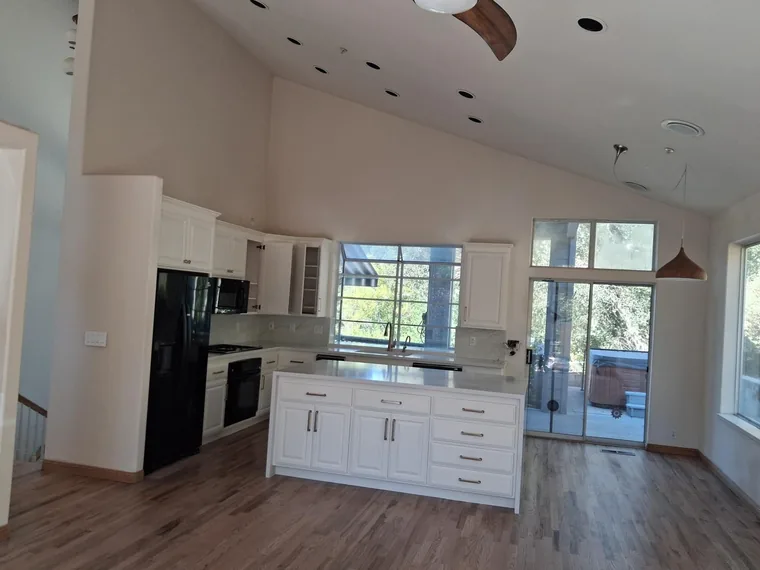 Open kitchen with white cabinetry, an island, wood flooring and tall windows