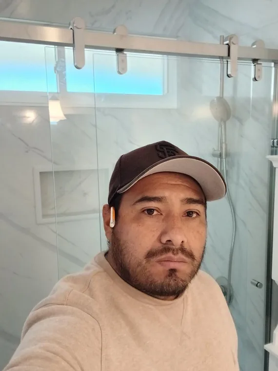 Person in front of a glass shower enclosure with marble-pattern wall tile and a high window