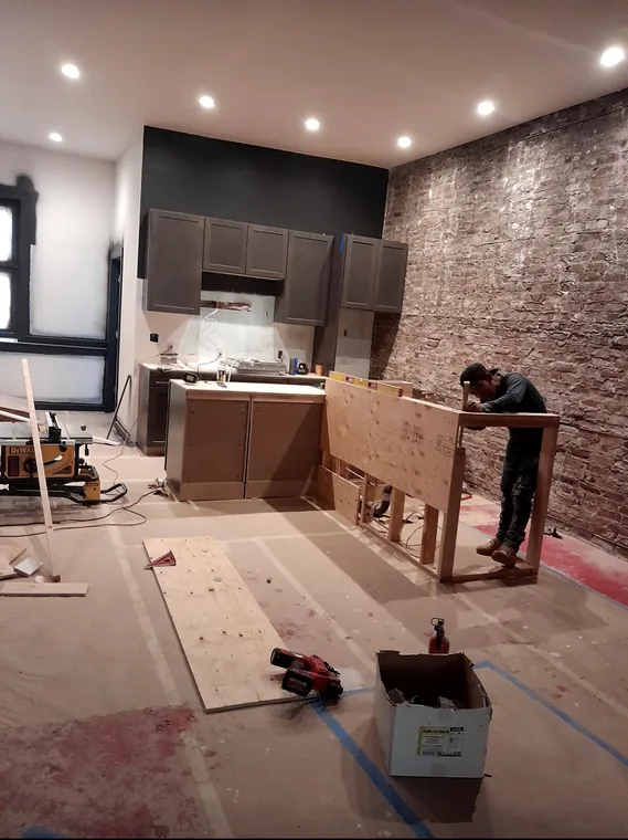 Kitchen cabinetry installation in progress beside an exposed brick wall
